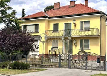 Elegante Villa mit gelber Fassade, rotem Ziegeldach und schmiedeeisernem Zaun im Vorgarten.