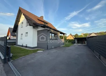 Modernes Einfamilienhaus mit gepflegtem Vorgarten und asphaltierter Auffahrt unter blauem Himmel.