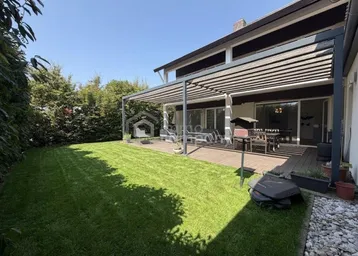 Gepflegter Garten mit Rasenfläche und einer überdachten Terrasse, ideal für entspannte Stunden im Freien.