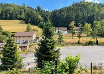 Weitläufige Landschaft mit grünen Hügeln und vereinzelten Häusern unter blauem Himmel.