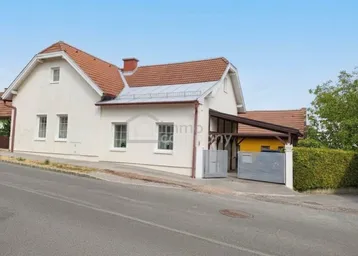 Weißes Einfamilienhaus mit Satteldach und Carport, von der Straße aus gesehen.