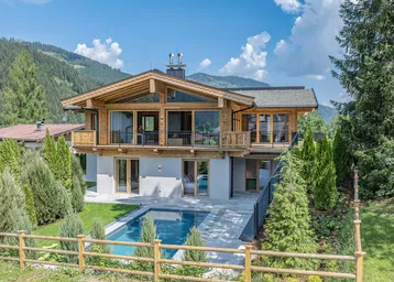 Modernes Chalet mit Holzfassade, großem Garten und privatem Pool in alpiner Berglandschaft.
