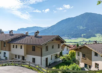 Traditionelle Häuser in alpiner Landschaft mit weitem Blick auf die Berge und grüne Täler.