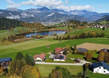 Panoramablick auf eine ländliche Landschaft mit See, Bergen und verstreuten Wohnhäusern.
