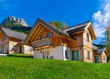 Traditionelle Holzhäuser in alpiner Landschaft mit Bergblick unter blauem Himmel.