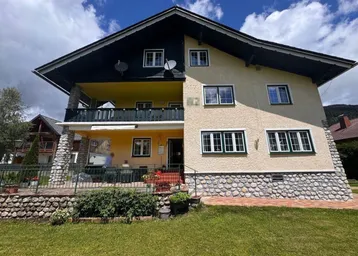 Traditionelles Haus mit mehreren Balkonen und einer möblierten Terrasse im Erdgeschoss, umgeben von einem gepflegten Garten.