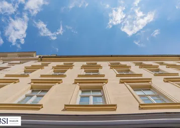 Blick nach oben auf die Fassade eines Altbaus mit vielen Fenstern unter einem blauen Himmel mit Wolken.