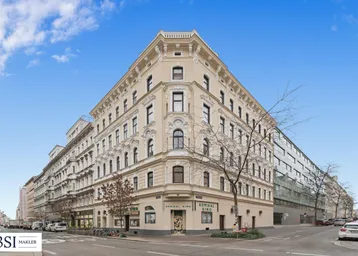 Historisches Eckgebäude mit reich verzierter Fassade und Geschäften im Erdgeschoss unter blauem Himmel.