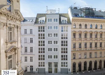 Modernes Wohngebäude mit vielen Fenstern, umgeben von historischen Altbauten in der Stadt.