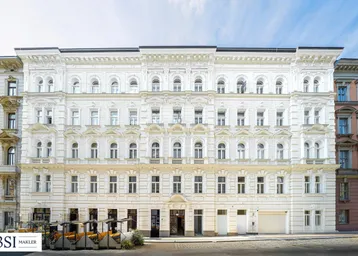 Weißes, historisches Gebäude mit reich verzierter Fassade und vielen Fenstern unter blauem Himmel.