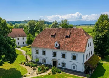 Historisches Anwesen mit weitläufigen Grünflächen und ländlicher Umgebung unter blauem Himmel.