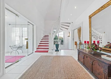 Heller Eingangsbereich mit eleganter Wendeltreppe, Fliesenboden und großem Spiegel.