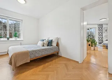 Gemütliches Schlafzimmer mit hellem Fischgrätparkett und Blick ins Grüne durch das Fenster.