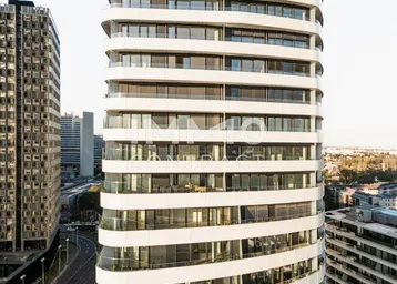 Moderne Hochhausfassade mit geschwungenen Balkonen und großen Fenstern in urbaner Umgebung.