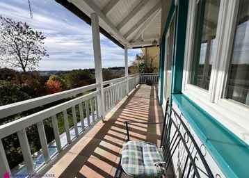 Langer Balkon mit Holzgeländer und weitem Blick über die hügelige Landschaft, sonnig und offen.