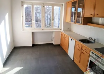 Küche mit Holzschränken, Fliesenboden, Fenster und integrierten Geräten.
