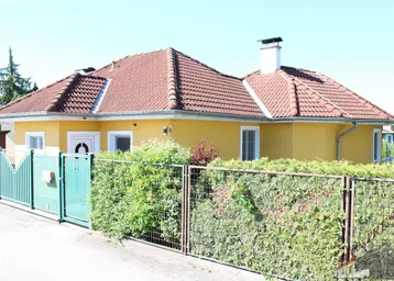 Gelbes Einfamilienhaus mit rotem Ziegeldach, grüner Hecke und Vorgarten.
