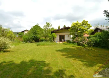 Weitläufiger Garten mit Rasenfläche und blühenden Büschen vor einem charmanten Einfamilienhaus.