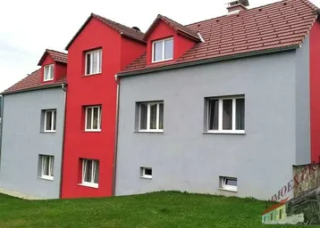 Mehrfamilienhaus mit markanter rot-grauer Fassade und Satteldach, umgeben von Grünflächen.