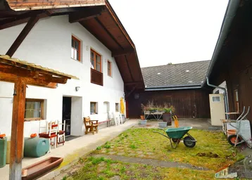 Ländlicher Innenhof mit Sitzgelegenheiten und Zugang zu den Gebäuden, umgeben von Grünflächen.