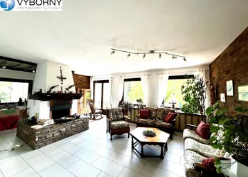 Geräumiges Wohnzimmer mit Kamin, hellen Fliesen und traditioneller Einrichtung, umgeben von Fenstern.