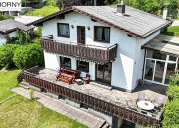 Freistehendes Haus mit großzügiger Terrasse, Balkon und integriertem Wintergarten in grüner Umgebung.