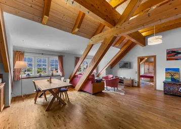 Geräumiger Wohn- und Essbereich mit Holzbalken, Parkettboden und Bergblick durch die Fenster.