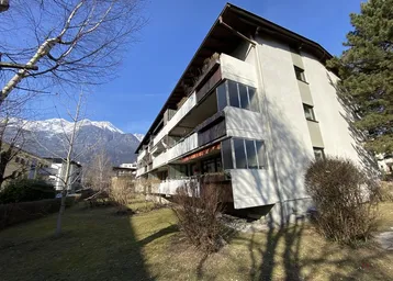 Mehrfamilienhaus mit Balkonen und Blick auf die umliegende Berglandschaft unter blauem Himmel.