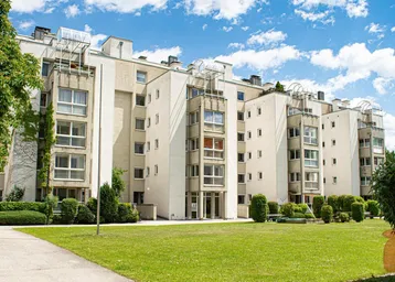 Modernes Mehrfamilienhaus mit gepflegter Grünanlage und blauer Himmel an einem sonnigen Tag.