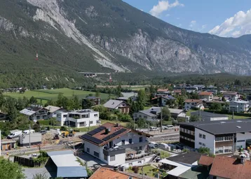 Panoramablick auf eine Wohnsiedlung mit Bergen im Hintergrund und einem Tal.