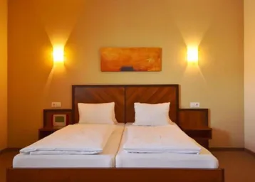 Helles Schlafzimmer mit zwei Einzelbetten, Holzkopfteil und warmen Wandleuchten.