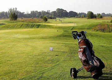 Weitläufiger Golfplatz mit grünen Fairways und Bäumen unter blauem Himmel.