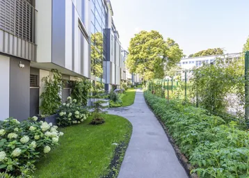 Schöner Gartenweg zwischen modernen Gebäuden mit gepflegten Grünflächen und blühenden Sträuchern.