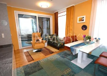 Heller Wohn- und Essbereich mit Holzboden, farbenfrohem Teppich und Zugang zum Balkon.