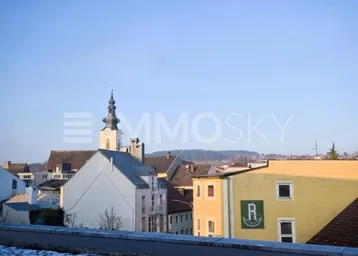 Panoramablick über eine charmante Stadt mit Kirchturm und grünen Hügeln im Hintergrund.