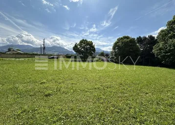 Weitläufiges grünes Grundstück mit Blick auf die umliegenden Berge unter blauem Himmel.
