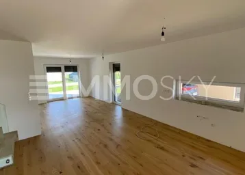 Helles, leeres Wohnzimmer mit Holzboden, großen Fenstern und Zugang zur Terrasse.