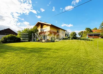 Freistehendes Haus mit großem grünen Garten und Balkon unter blauem Himmel.
