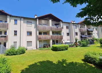 Mehrfamilienhaus mit mehreren Balkonen und einer gepflegten Grünfläche im Vordergrund unter blauem Himmel.