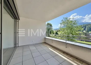 Geräumiger Balkon mit Fliesenboden, Blick ins Grüne und auf die Berge unter blauem Himmel.