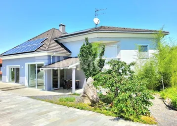 Modernes Einfamilienhaus mit heller Fassade, Solaranlage auf dem Dach und gepflasterter Auffahrt.