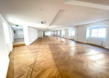 Großer, heller Raum mit Fischgrätparkett und vielen Fenstern, ideal für Büronutzung.