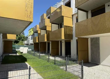Moderne Wohnanlage mit markanten goldenen Balkonen und gepflegten Grünflächen im Außenbereich.