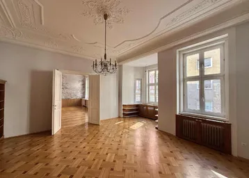 Helles Wohnzimmer mit Fischgrätparkett, hohen Stuckdecken und großen Fenstern.