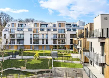 Moderne Wohngebäude mit weißer Fassade, Holzverkleidung und begrünten Außenanlagen unter blauem Himmel.