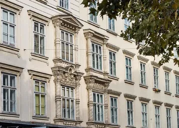 Detailansicht einer historischen Fassade mit reich verzierten Fenstern und Stuckelementen.