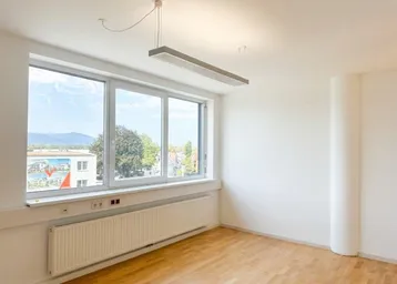 Leerer Büroraum mit großen Fenstern, Holzboden und Blick auf die Umgebung und Berge.