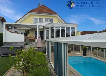 Großzügiger Außenbereich mit Hausfassade, überdachtem Pool und gepflegtem Garten.