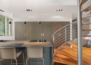 Moderne Küche mit Kochinsel, integrierten Geräten und einer eleganten Wendeltreppe im Hintergrund.