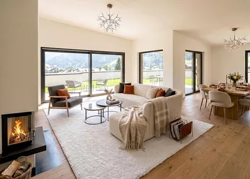 Heller, offener Wohn- und Essbereich mit Kamin, Holzboden und Zugang zur Terrasse mit Bergblick.